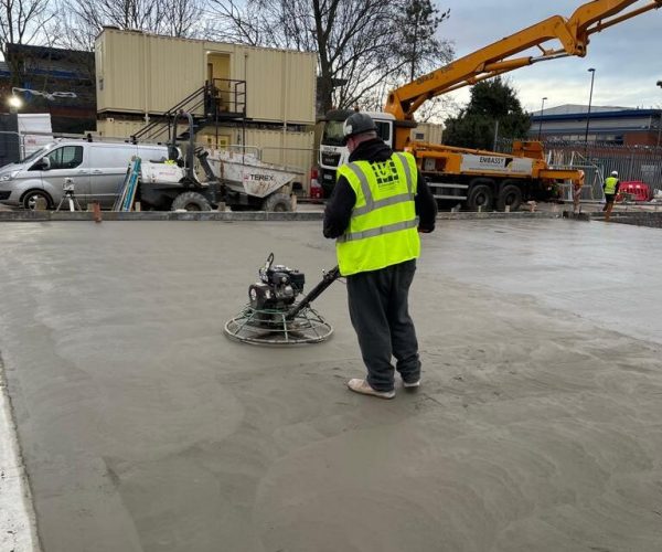 Concrete flooring works with workers preparing and finishing slab surface